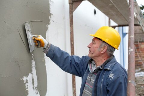A man painting a wall with a roller, illustrating tips for choosing stucco finishes in San Jose, CA